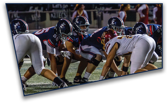 Several people in football uniforms are crouched in a line on a field, preparing for a play during a game. Description generated by AI