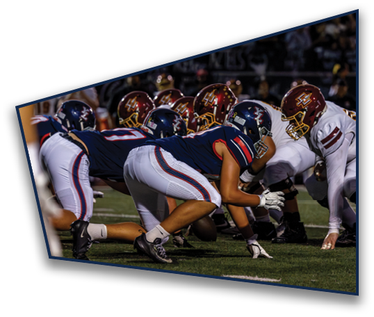 People in athletic gear are crouched in a ready position on a football field, preparing for a play. Description generated by AI