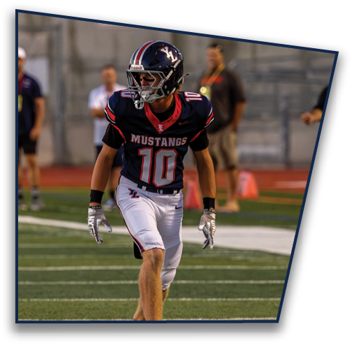 A person wearing a Mustangs football uniform with the number 10 is standing on a football field with blurred people and equipment in the background. Description generated by AI