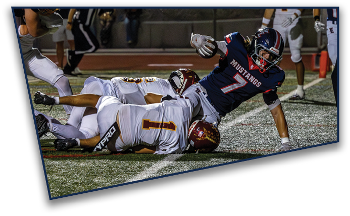A group of people in football uniforms are engaged in a play on a field with one person in a dark uniform being tackled by two people in white uniforms while a referee watches nearby. Description generated by AI