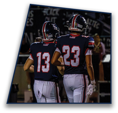 Two people wearing football uniforms with numbers 13 and 23 walk side by side on a field at night. Description generated by AI