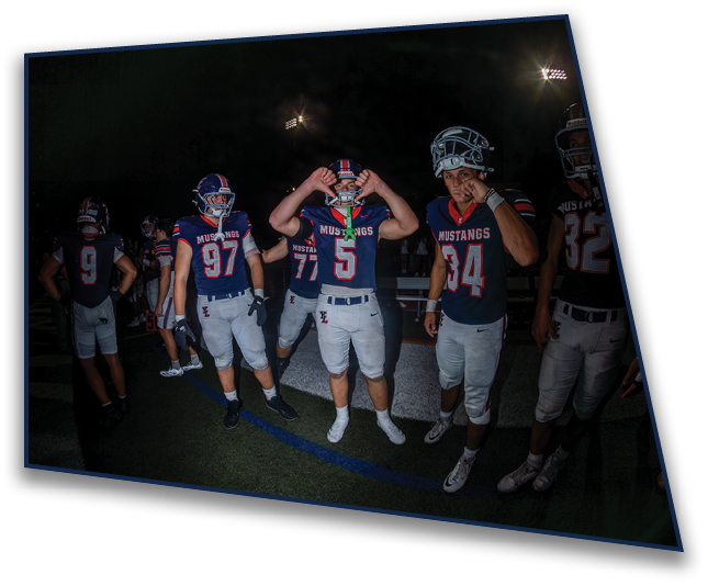 People wearing football helmets are partially visible at the bottom of the image against a dark background with stadium lights. Description generated by AI