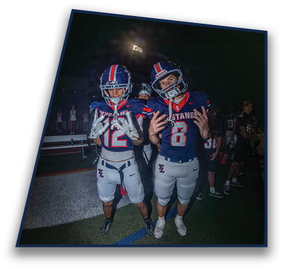 Two people wearing football helmets with red, white, and blue stripes are looking up against a dark night sky with a bright stadium light in the background. Description generated by AI