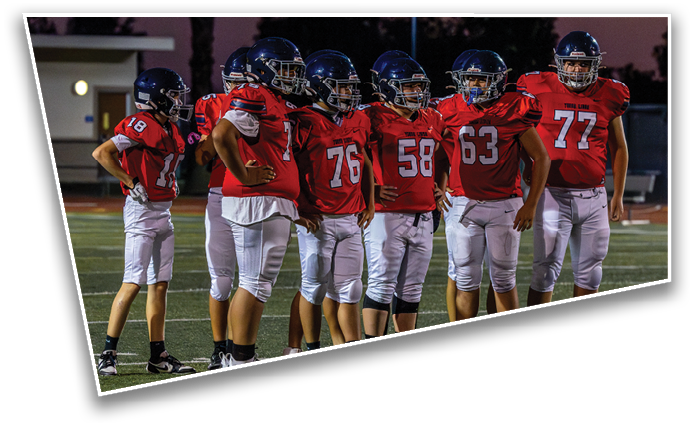 A group of people wearing red football jerseys and helmets stand together on a field at dusk. Description generated by AI