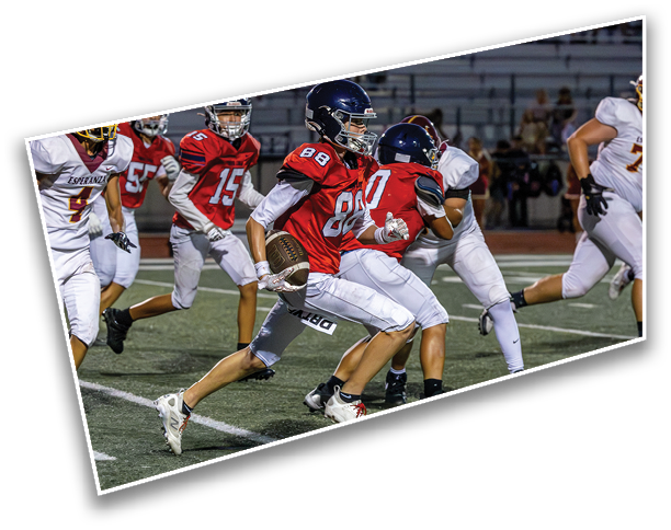 People in football uniforms are actively running on a field during a game, with one person holding the ball and others in pursuit. Description generated by AI