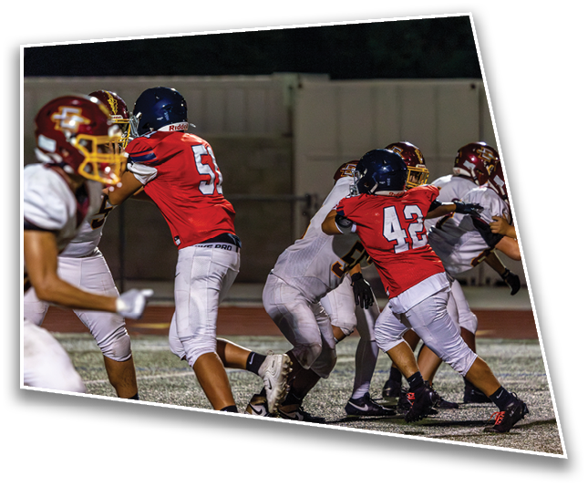 People wearing football uniforms are engaged in a play on a turf field during a game. Description generated by AI