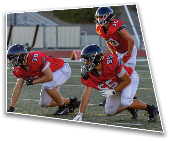 Three people in red football jerseys and helmets are crouched on a field preparing for a play during a game. Description generated by AI