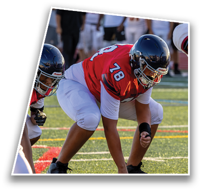 People in football uniforms and helmets are crouched in a ready position on a field with others standing in the background. Description generated by AI