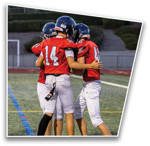 Three people wearing red football jerseys and white pants are embracing on a football field. Description generated by AI