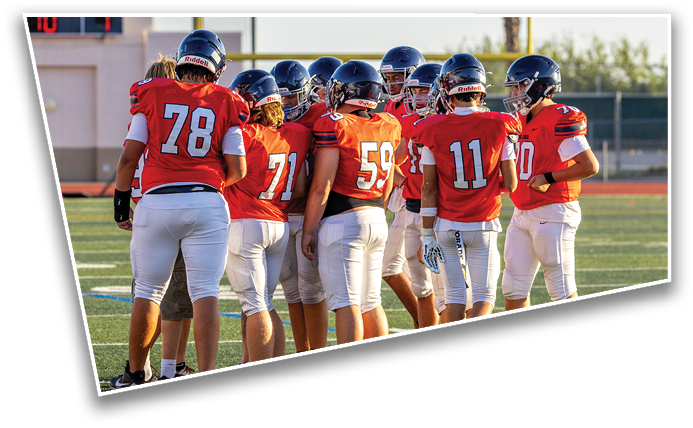 A group of people wearing red football jerseys and helmets are gathered on a football field during daylight. Description generated by AI