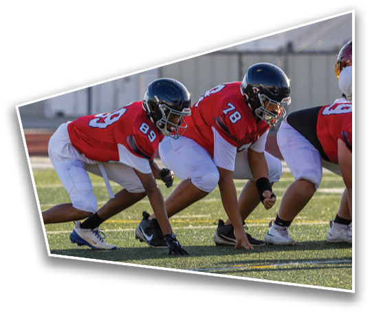 Three people in red and white football uniforms and helmets are crouched in a ready position on a grassy field. Description generated by AI