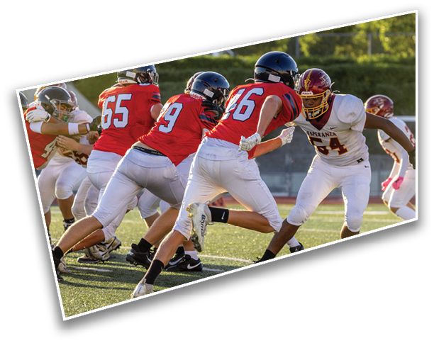 Several people wearing helmets and sports uniforms are engaged in a football game on a grassy field. Description generated by AI