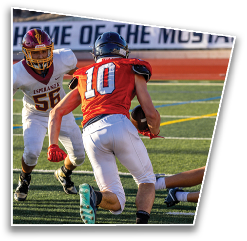 A person wearing a red jersey with the number 10 is running with a football while another person in a white jersey with the number 56 approaches on a football field. Description generated by AI