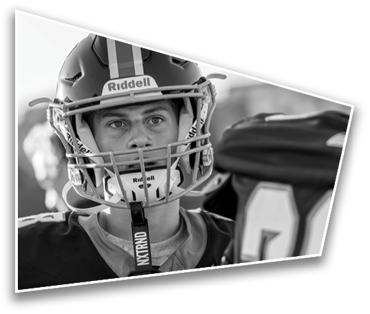 A person wearing a football helmet and uniform looks focused while standing next to another person in similar gear. Description generated by AI