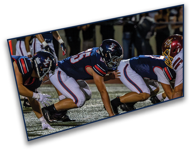 Three people in football uniforms are crouched in a ready position on a field during a game. Description generated by AI