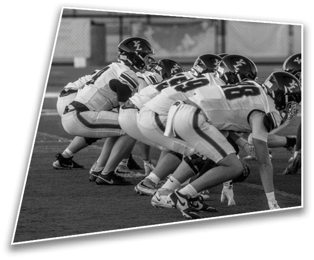 A group of football players in uniform and helmets are crouched in a line on a field, preparing for a play. Description generated by AI