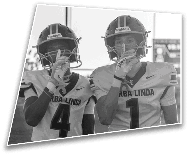Two people wearing football helmets are partially visible at the bottom of the image with a light pole and clear sky in the background. Description generated by AI