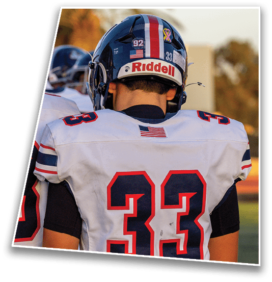 A person wearing a football helmet with red, white, and blue stripes, a pink ribbon decal, and the brand name Riddell on the back is seen from behind. Description generated by AI