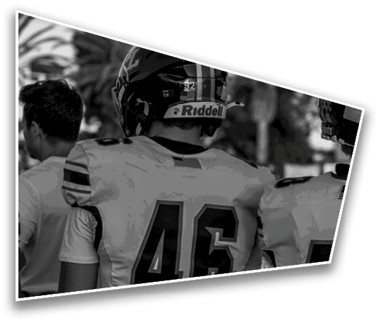 Two people wearing football helmets and jerseys with numbers 46 and 5 are standing next to each other outdoors. Description generated by AI
