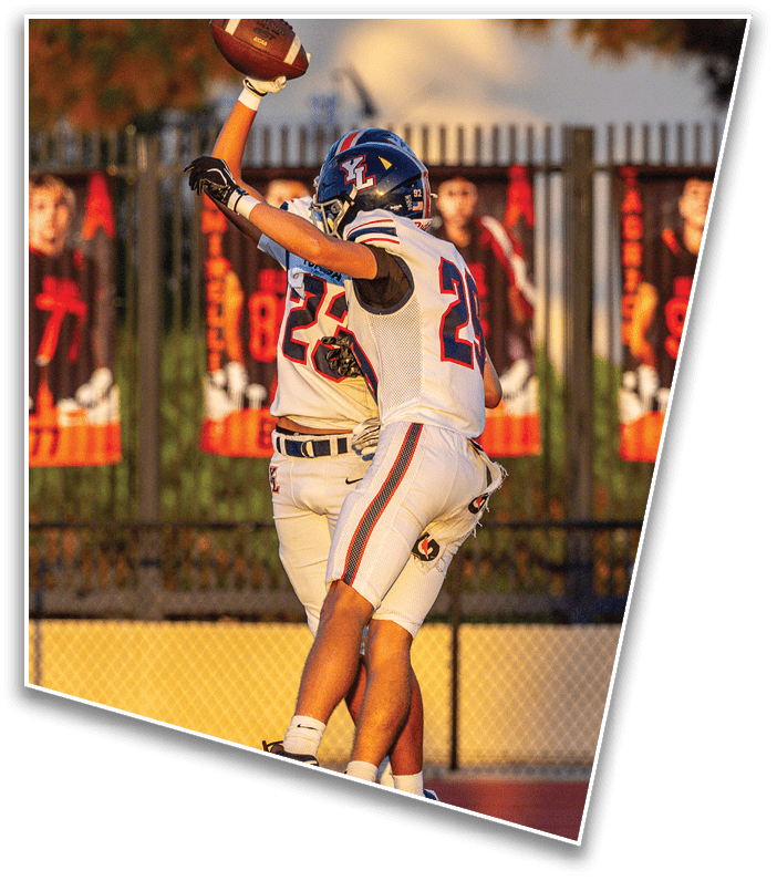 Two people in football uniforms are celebrating on a field with one holding a football raised above their head. Description generated by AI