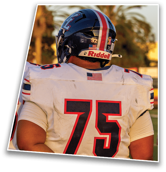 A person wearing a white football jersey with the number 75 and a dark helmet is standing outdoors. Description generated by AI