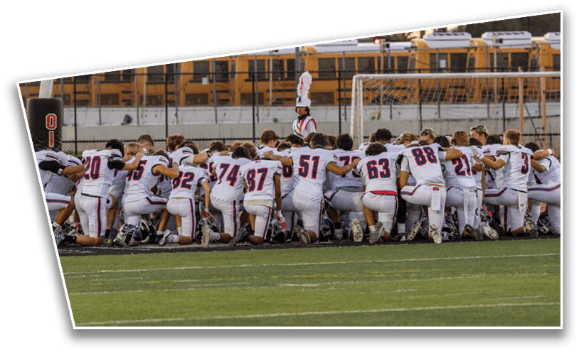 A group of people wearing white sports uniforms are kneeling together on a football field near the goalpost. Description generated by AI
