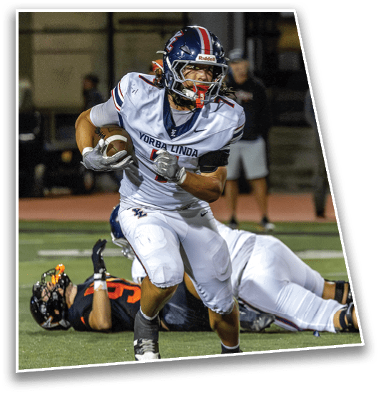 A person in a white football uniform with “Yorba Linda" on the jersey is running with a football while another person in a black and orange uniform lies on the ground behind them on a football field. Description generated by AI