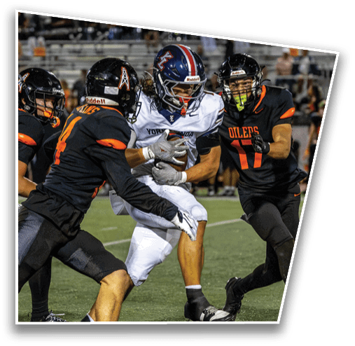 Three football players in action on a field with two players in black and orange uniforms attempting to tackle a player in a white uniform holding the ball. Description generated by AI
