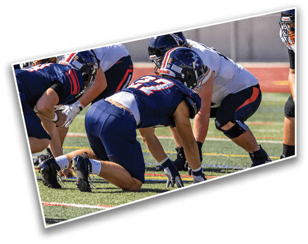 Several football players in helmets and uniforms are crouched on a field, preparing for a play. Description generated by AI