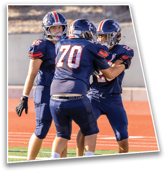 Three people in football uniforms and helmets are standing on a field with one person embracing another while the third looks on. Description generated by AI