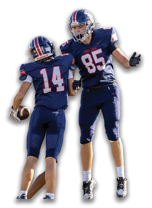 Two people in football uniforms are celebrating, with one holding a football and the other jumping with arms outstretched. Description generated by AI