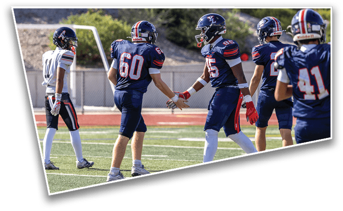 People in football uniforms are on a field with two players in dark blue uniforms giving a handshake while others stand nearby. Description generated by AI