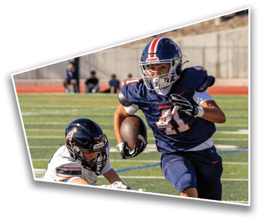 A person in a blue football uniform with the number 41 is running with the ball while another person in a white uniform is attempting to tackle them on a football field. Description generated by AI