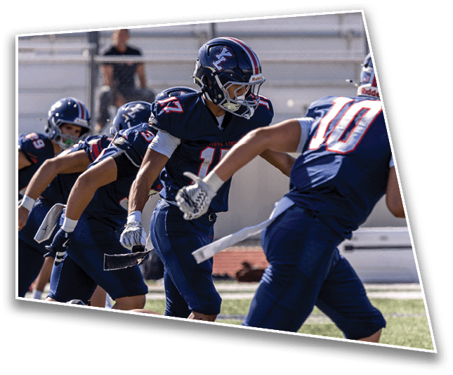 People wearing football helmets and uniforms are on a field with empty bleachers in the background. Description generated by AI