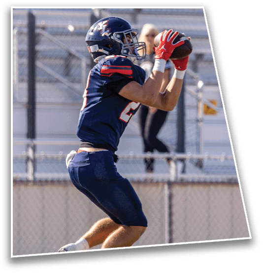 A person wearing a dark blue sports uniform is jumping or running on a field with a chain-link fence in the background. Description generated by AI