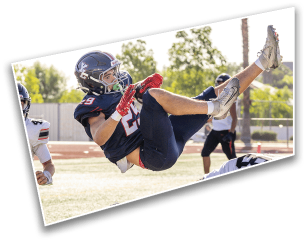 A person in a football uniform is airborne, performing a backflip or falling backward on a football field while other players and a referee are nearby. Description generated by AI