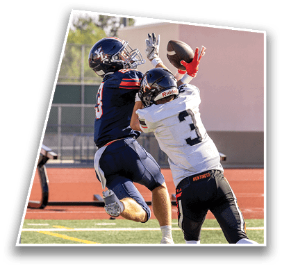 Two people in football uniforms and helmets are jumping and reaching to catch a football on an outdoor field. Description generated by AI