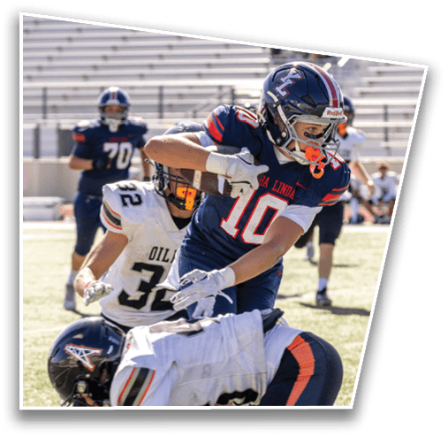 Three people in football uniforms are engaged in a play on a sunlit field with one player in a white jersey bent forward and two others in white and blue jerseys closely interacting. Description generated by AI
