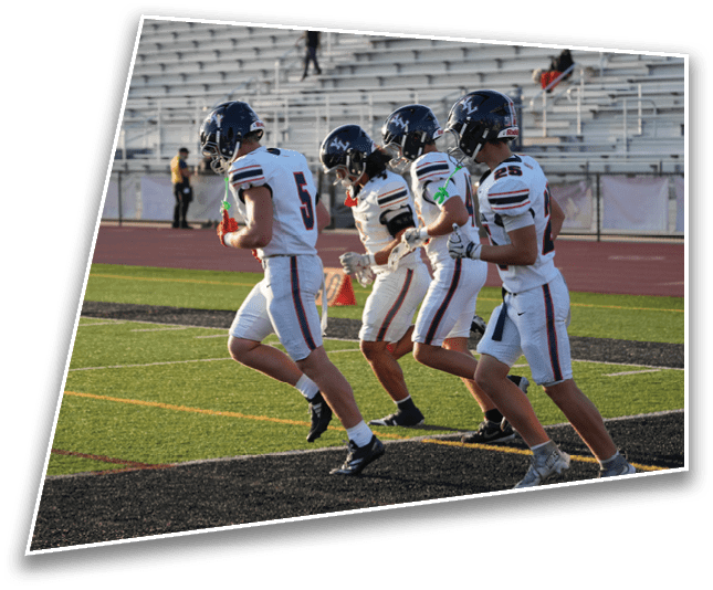 Four people in sports uniforms are running on a football field near the end zone. Description generated by AI