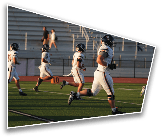 Three people in football uniforms and helmets are running on a field with empty bleachers in the background. Description generated by AI