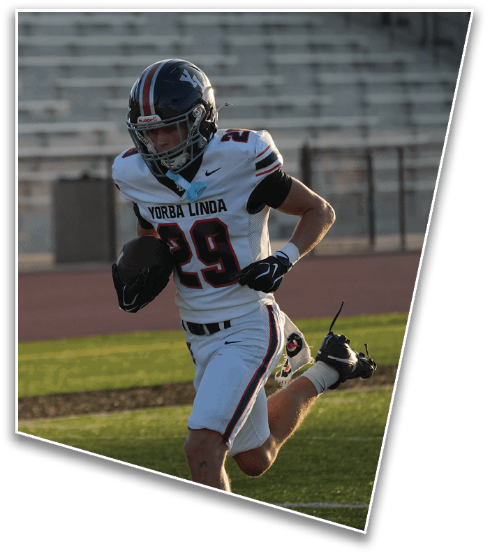 An adult in a white football uniform with the number 29 is running on a field while holding a football. Description generated by AI