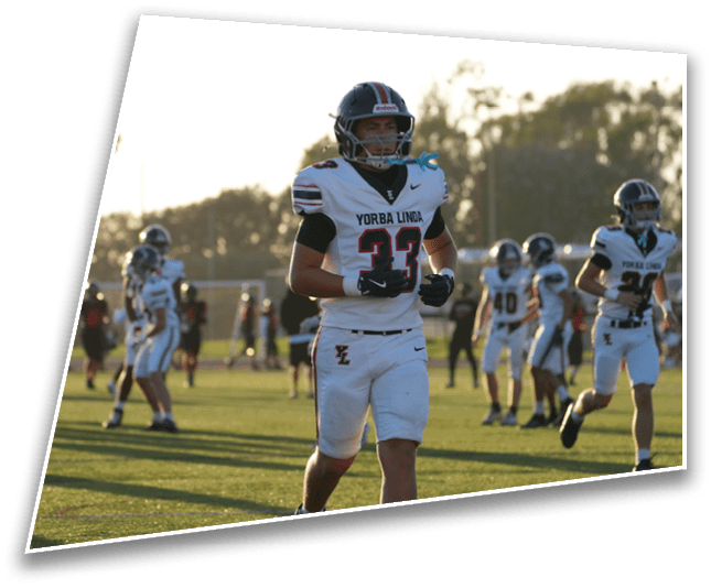 People in football uniforms are on a field during a game or practice with one person prominently walking toward the camera. Description generated by AI