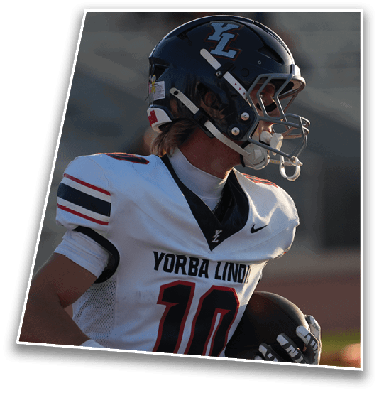 A person wearing a football helmet and a white jersey with “Yorba Linda" and the number 10 printed on it is holding a football and looking to the side. Description generated by AI