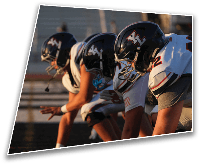 Several people in football uniforms and helmets are crouched in a ready position on a field, preparing for a play. Description generated by AI