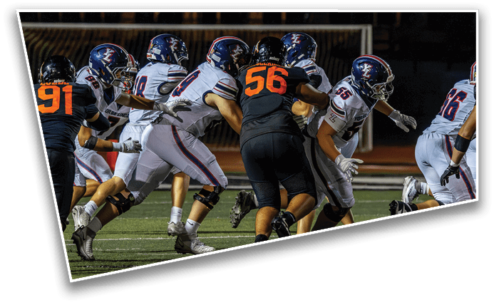 Several football players in white and black uniforms are engaged in a play on a field under stadium lights. Description generated by AI