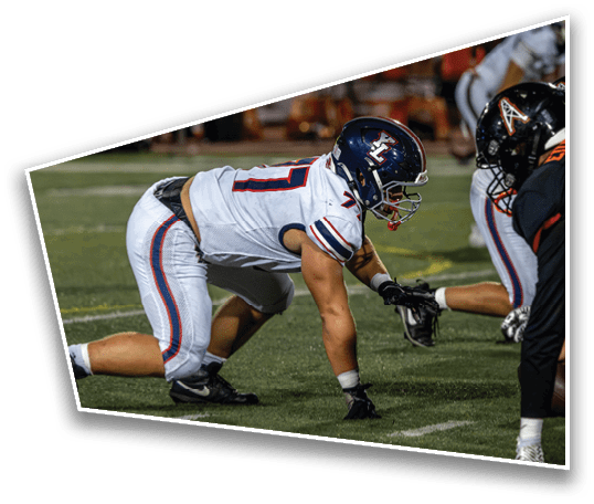 Two people in football uniforms are crouched facing each other on a field, ready for a play. Description generated by AI