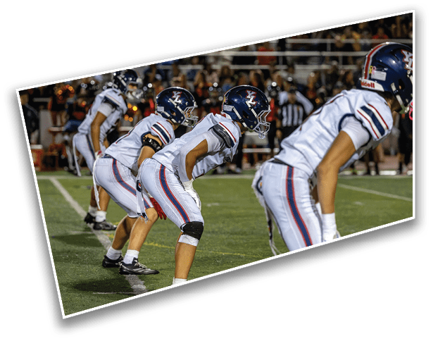 A group of people in football uniforms and helmets are crouched in a ready position on a field during a game. Description generated by AI