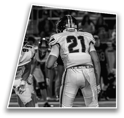A person wearing a football uniform with the number 21 is standing on a field preparing for a play during a game with other players and spectators in the background. Description generated by AI