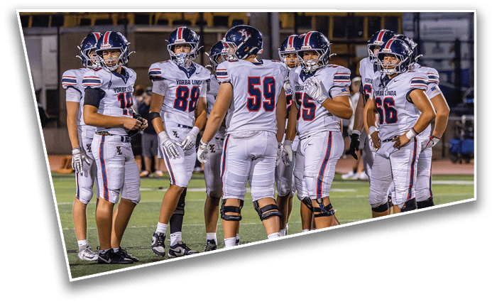 A group of six people wearing football uniforms and helmets are standing together on a field, appearing to discuss strategy during a game. Description generated by AI