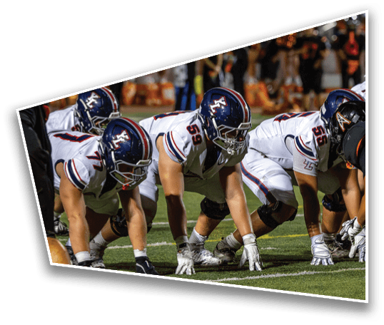Several people in football uniforms and helmets are crouched in a ready position on a football field during a game. Description generated by AI